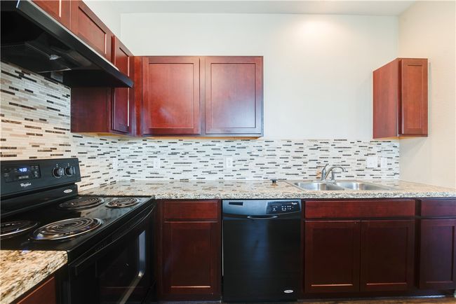 Kitchen with ventilation hood, dark brown cabinets, a sink, black appliances, and tasteful backsplash | Image 4