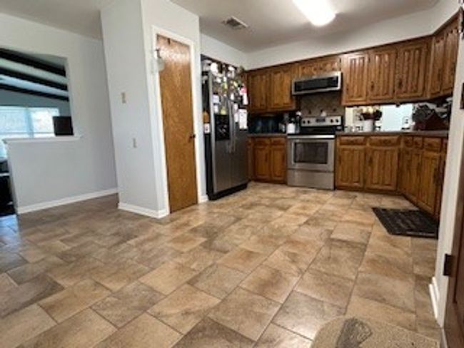 Kitchen with appliances with stainless steel finishes, baseboards, decorative backsplash, exhaust hood, and light stone finish floors | Image 9