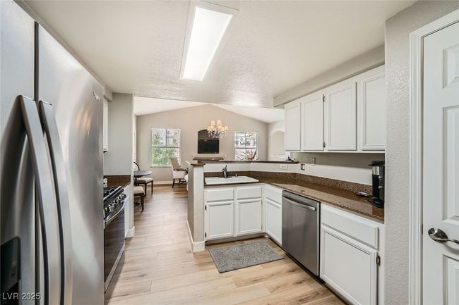 Kitchen with white cabinets, stainless steel appliances, a sink, dark countertops, and a chandelier | Image 7
