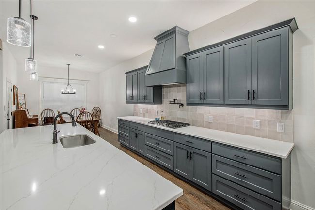 Kitchen with light stone counters, gray cabinets, backsplash, stainless steel gas cooktop, and a sink | Image 10