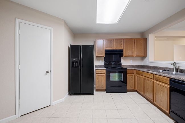 Kitchen featuring black appliances, range hood, light tile patterned floors, and dark countertops | Image 5