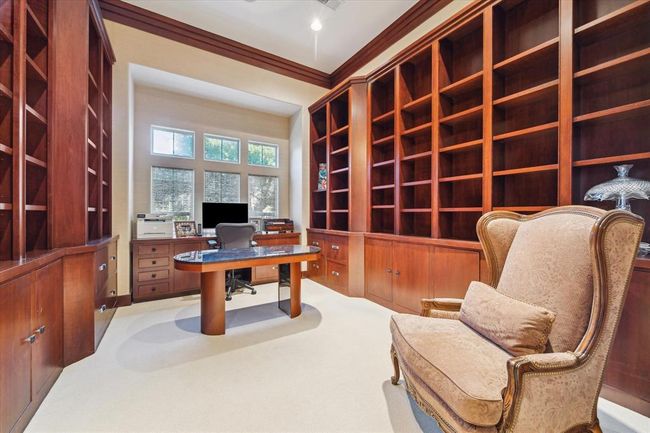 This photo showcases a spacious home office with elegant built-in wooden bookshelves. Natural light streams through multiple windows, creating a bright and inviting workspace. | Image 16