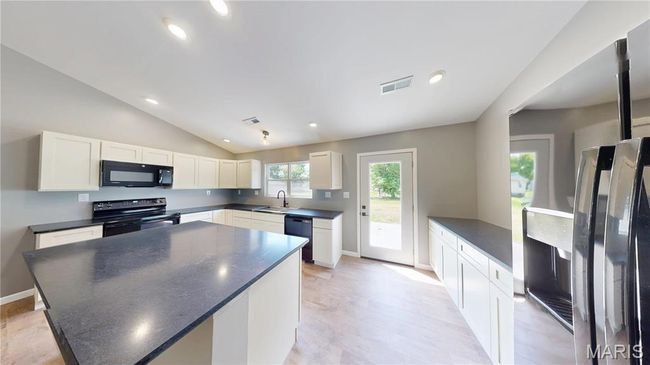 Kitchen with black appliances, dark countertops, vaulted ceiling, white cabinets, and light wood-style floors | Image 10