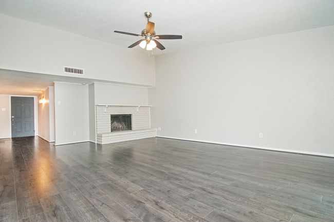 Unfurnished living room featuring ceiling fan, a brick fireplace, a towering ceiling, and dark wood-type flooring | Image 8
