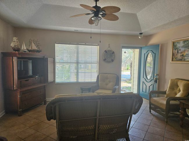 Tiled living area with a textured ceiling, a ceiling fan, a raised ceiling, and lofted ceiling | Image 6