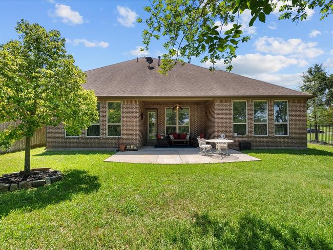 This photo showcases a cozy backyard with a well-maintained lawn and a brick house featuring large windows. There's a patio area with seating, perfect for outdoor relaxation or entertaining. Lush greenery surrounds the space, adding privacy and charm. | Image 45