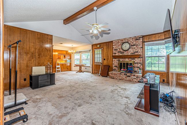 Living area with ceiling fan with notable chandelier, wooden walls, carpet, and a brick fireplace | Image 19