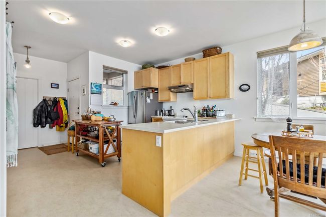 Kitchen with light countertops, freestanding refrigerator, a peninsula, light brown cabinets, and under cabinet range hood | Image 9