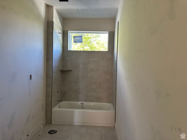 Bathroom with baseboards, tile patterned floors, a textured ceiling, and washtub / shower combination | Image 15