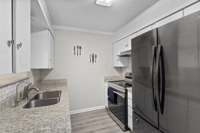 Kitchen with backsplash, a sink, freestanding refrigerator, electric stove, and under cabinet range hood | Image 15