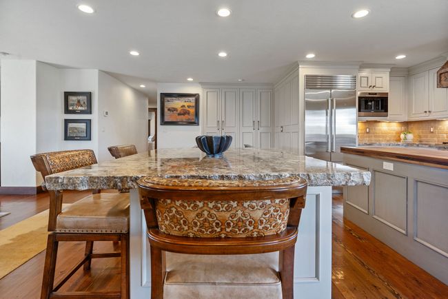 Kitchen featuring a kitchen breakfast bar, stainless steel built in refrigerator, a center island, wood finished floors, and backsplash | Image 25
