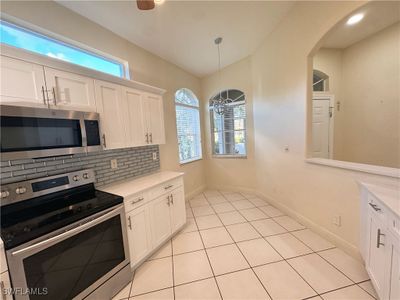 Kitchen with decorative backsplash, white cabinetry, stainless steel appliances, and hanging light fixtures | Image 3