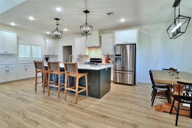 Kitchen with light countertops, light wood-style floors, a center island with sink, appliances with stainless steel finishes, and custom exhaust hood | Image 9