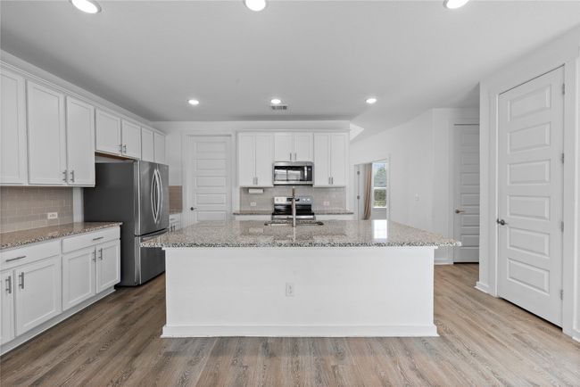 Kitchen featuring white cabinets, a center island with sink, light wood-type flooring, and appliances with stainless steel finishes | Image 16