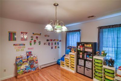 Playroom with light hardwood / wood-style floors, a baseboard radiator, and a chandelier | Image 2