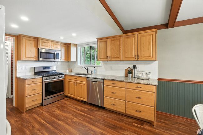 Kitchen featuring appliances with stainless steel finishes, light stone counters, decorative backsplash, dark wood-style floors, and a wainscoted wall | Image 9