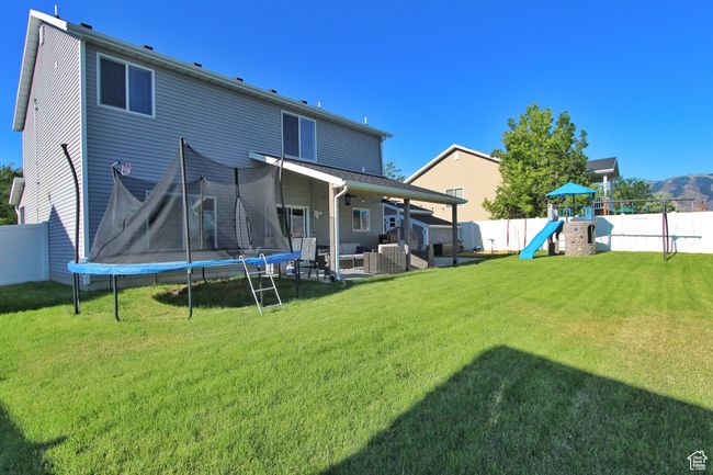 Back of property with a trampoline, a fenced backyard, a playground, a ceiling fan, and a patio | Image 24