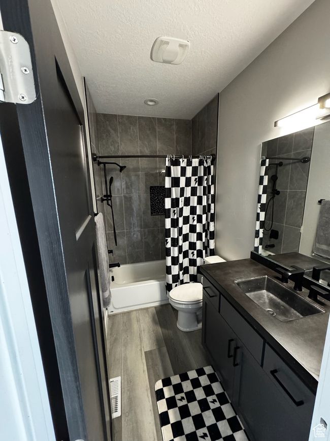 Full bathroom with vanity, shower / tub combo with curtain, wood finished floors, a textured ceiling, and toilet | Image 15