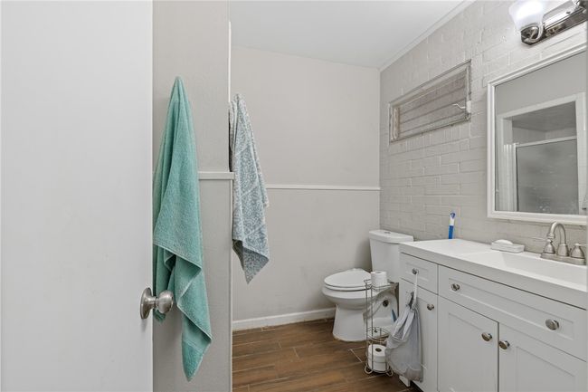 Bathroom featuring vanity, toilet, a shower with shower door, and brick wall | Image 14