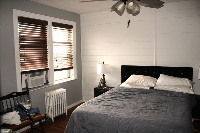 Bedroom with radiator heating unit, dark wood-style flooring, baseboards, and ceiling fan | Image 11