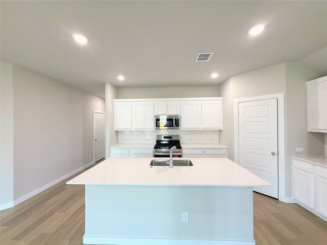 Kitchen featuring light wood-style flooring, appliances with stainless steel finishes, light countertops, a center island with sink, and white cabinets | Image 5