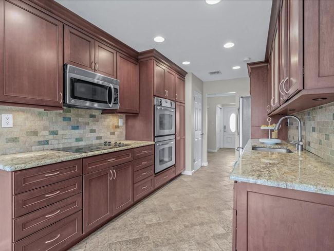 Kitchen featuring baseboards, backsplash, a sink, light stone countertops, and appliances with stainless steel finishes | Image 9