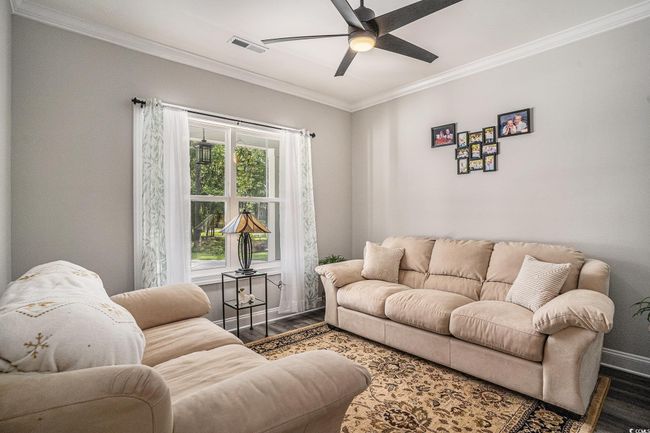 Living area with wood finished floors, crown molding, a ceiling fan, and baseboards | Image 5