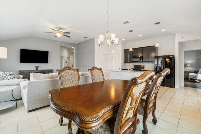 Dining area featuring ceiling fan with notable chandelier, visible vents, lofted ceiling, and light tile patterned floors | Image 11
