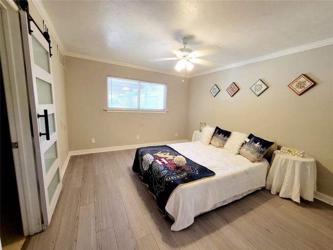 Bedroom with a barn door, ceiling fan, crown molding, and light hardwood / wood-style floors | Image 9
