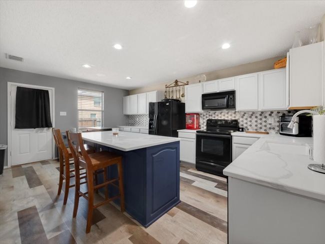 Kitchen with a kitchen island, backsplash, white cabinets, and black appliances | Image 11