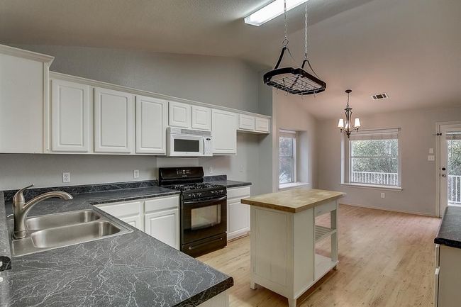 Kitchen with white microwave, gas stove, a sink, lofted ceiling, and white cabinetry | Image 8
