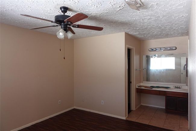 Spacious master bedroom featuring elegant laminate flooring, an en-suite vanity area, and a modern ceiling fan for ultimate comfort. | Image 10