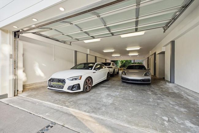 Wide-angle view of an oversized, fully enclosed garage with a modern frosted-glass door lifted open, revealing a clean and well-lit space that comfortably houses multiple luxury vehicles. The polished concrete floor and recessed lighting give the garage a refined, showroom-quality feel. With generous width and depth, this space is ideal for vehicle storage, workshop use, or flexible recreational space—highlighting its rare combination of function and style. | Image 37