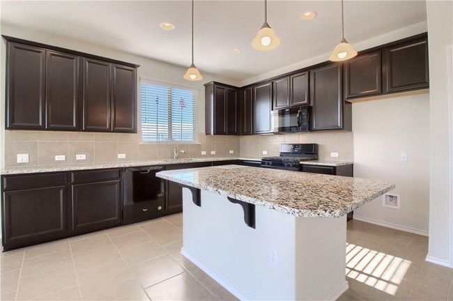 Kitchen featuring black appliances, dark brown cabinetry, a breakfast bar area, decorative backsplash, and a kitchen island | Image 9