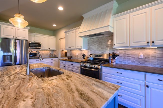 Kitchen featuring stainless steel appliances, custom exhaust hood, a sink, dark stone counters, and white cabinets | Image 12