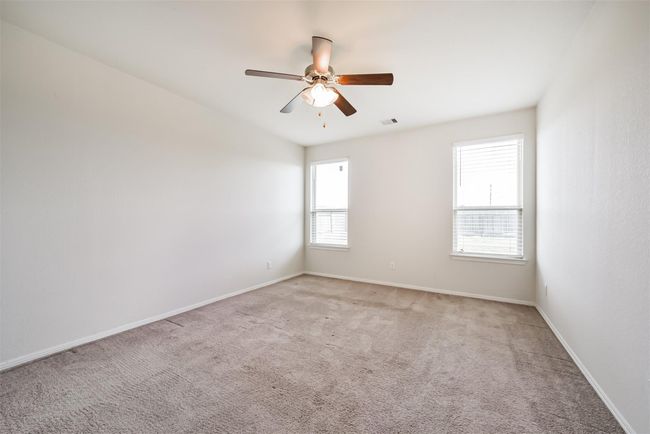 The primary bedroom is spacious and bright with neutral carpeting and walls. It features two windows for natural light and a ceiling fan for comfort. | Image 10