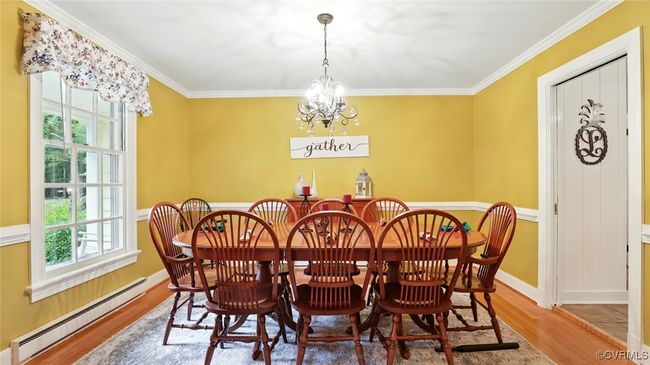 Dining space featuring a baseboard heating unit, healthy amount of natural light, wood finished floors, ornamental molding, and a chandelier | Image 48