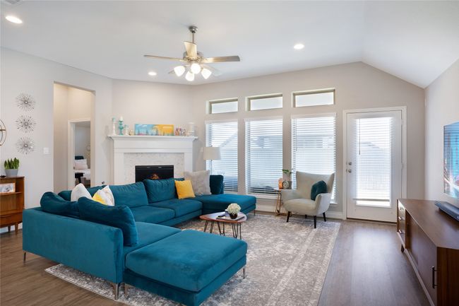 Living room with wood finished floors, a warm lit fireplace, a ceiling fan, and recessed lighting | Image 5