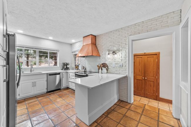 Kitchen featuring premium range hood, a peninsula, a sink, light countertops, and appliances with stainless steel finishes | Image 15