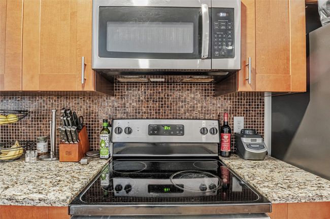 Kitchen featuring stainless steel appliances, decorative backsplash, and light stone counters | Image 5