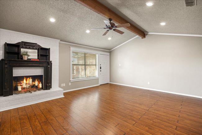 Open floor plan with warm wood laminate flooring and open views to front courtyard. Wood burning fireplace with raised hearth. | Image 10