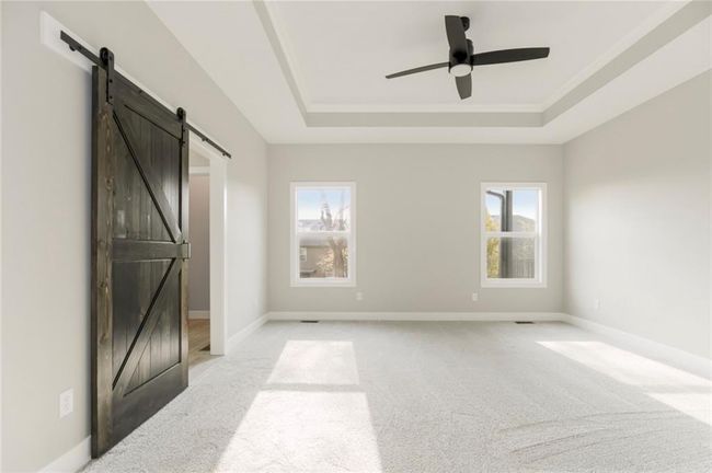 Unfurnished bedroom with a barn door, a raised ceiling, light colored carpet, and multiple windows | Image 8