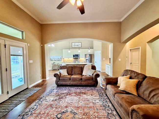 Living area with wood finished floors, arched walkways, crown molding, baseboards, and ceiling fan | Image 4
