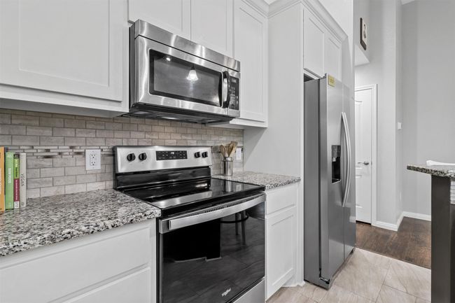 Kitchen featuring baseboards, light stone countertops, stainless steel appliances, tasteful backsplash, and white cabinetry | Image 8
