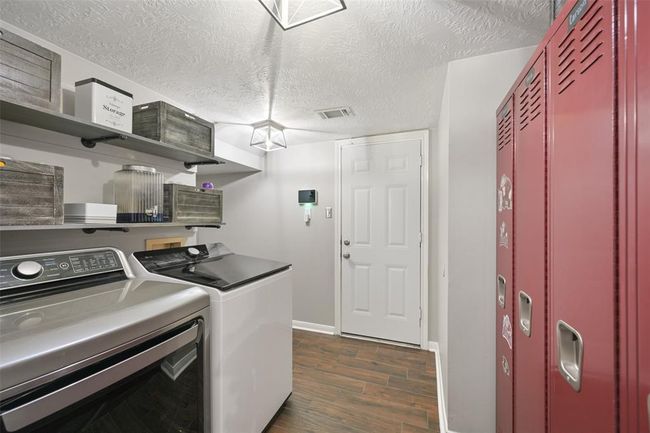 Well-organized laundry room with wood-look tile flooring, open shelving for storage, modern lighting, and a fun locker-style drop zone—both functional and stylish for daily routines. | Image 17