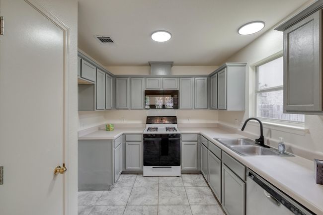 Kitchen featuring black microwave, gas range gas stove, gray cabinetry, stainless steel dishwasher, and light countertops | Image 12