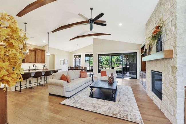 Living room featuring light wood-type flooring, beamed ceiling, high vaulted ceiling, a stone fireplace, and ceiling fan | Image 6
