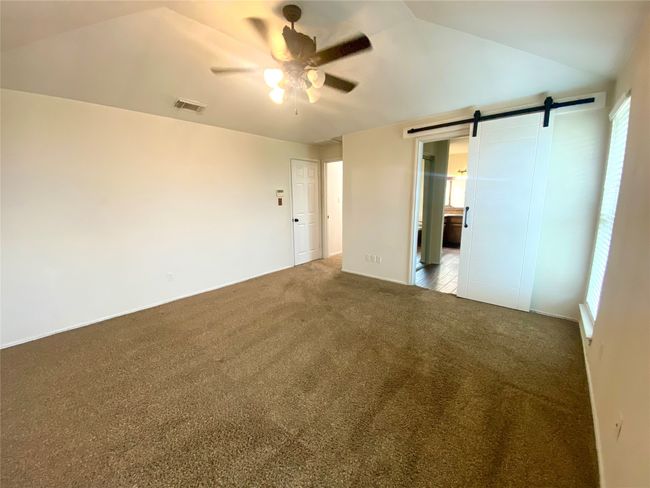 Primary bedroom with ceiling fan, barn door, and lofted ceiling | Image 12