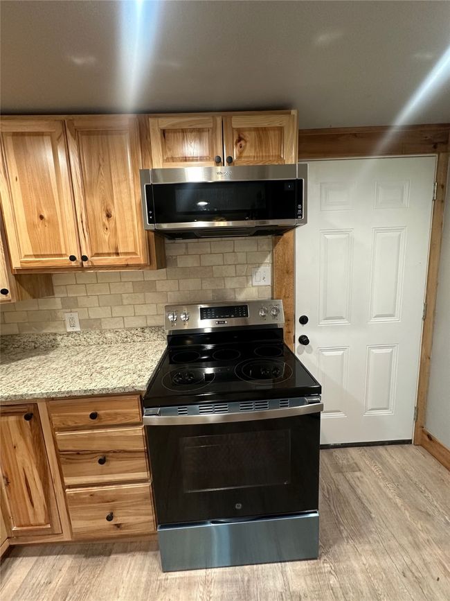 Kitchen with stainless steel microwave, light wood-style floors, range with electric cooktop, and decorative backsplash | Image 15
