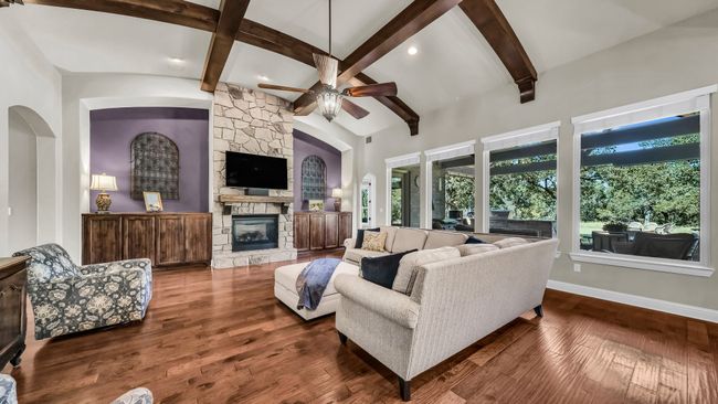 Living area with a ceiling fan, a stone fireplace, beam ceiling, wood finished floors, and recessed lighting | Image 9